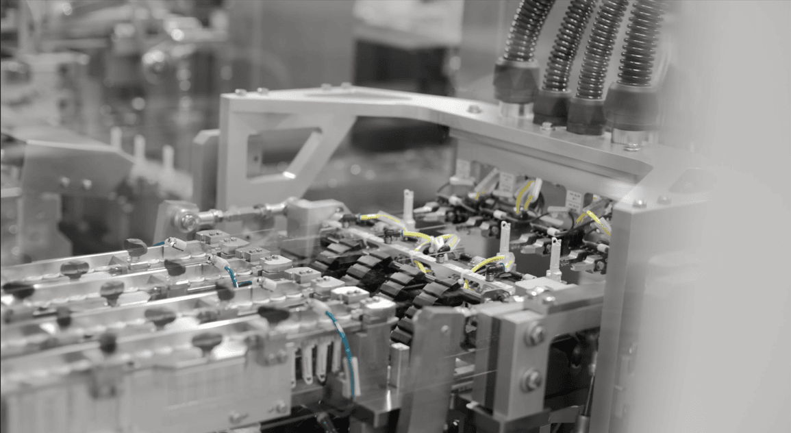 A close-up, grayscale view of a complex automated assembly line used for manufacturing medical devices.