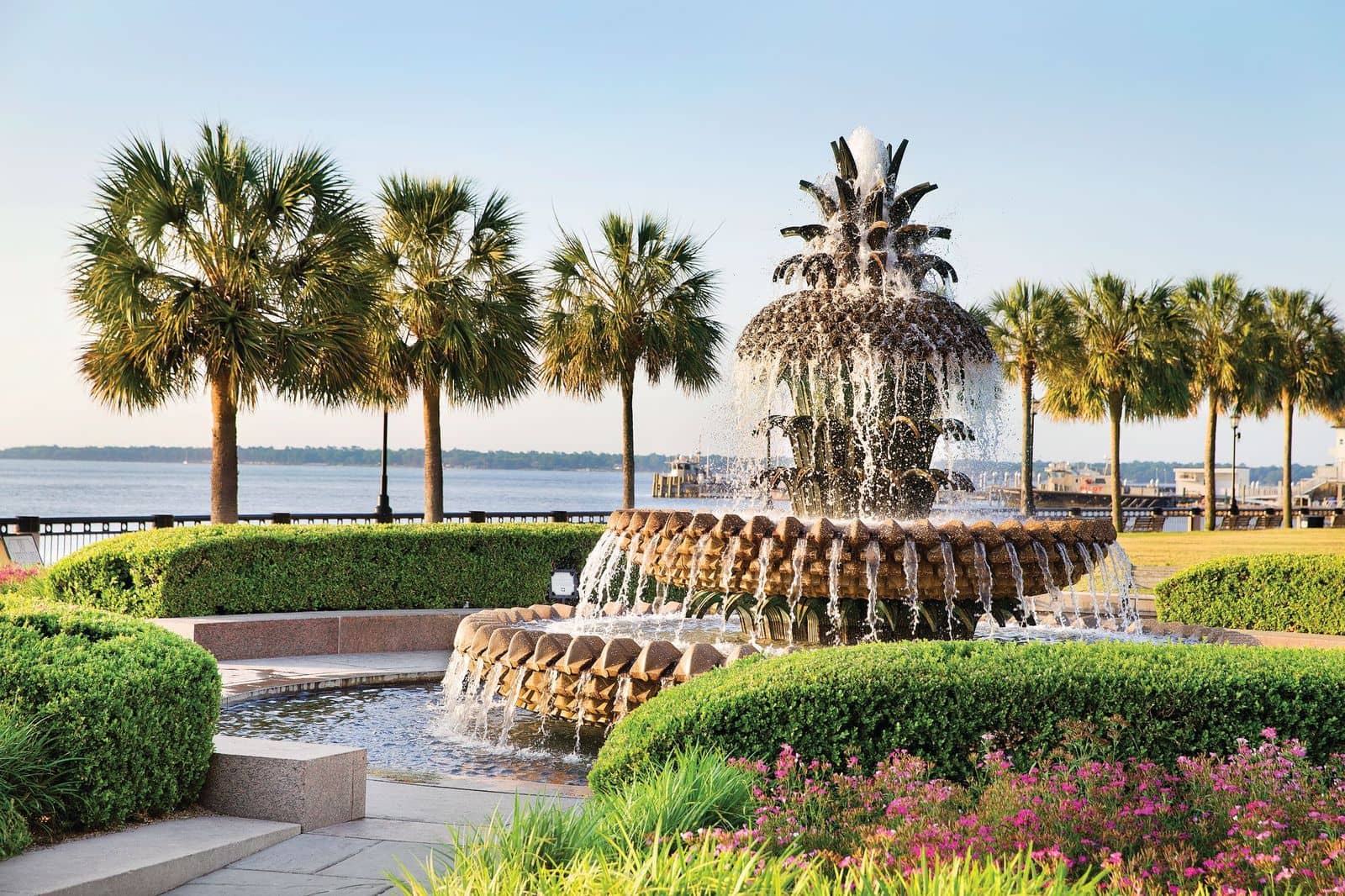 The Pineapple Fountain in Joe Riley Waterfront Park, Charleston, South Carolina, surrounded by palm trees and greenery overlooking the harbor.