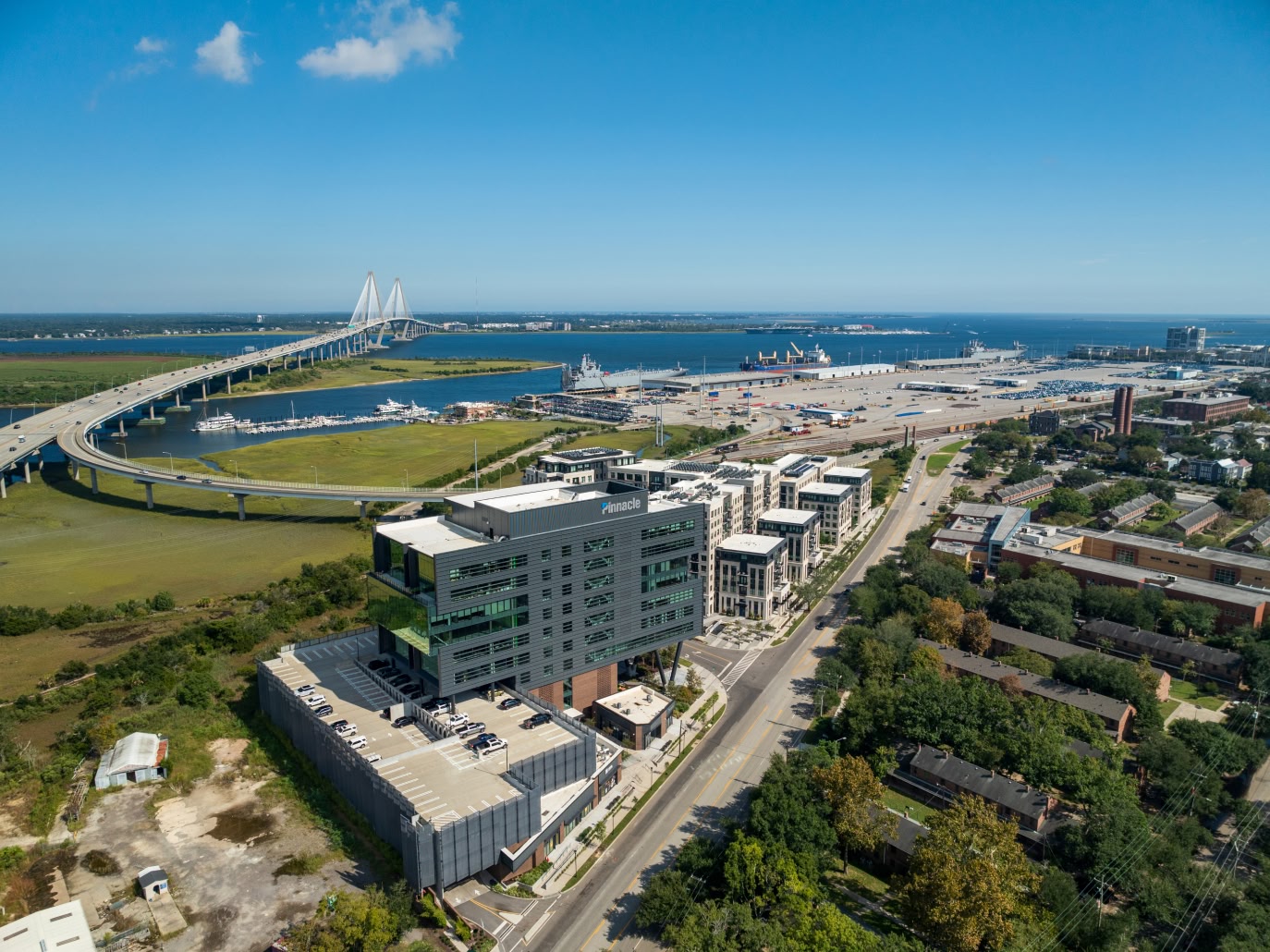 Aerial view of a coastal cityscape showing modern buildings, a prominent curved bridge, and a busy port.