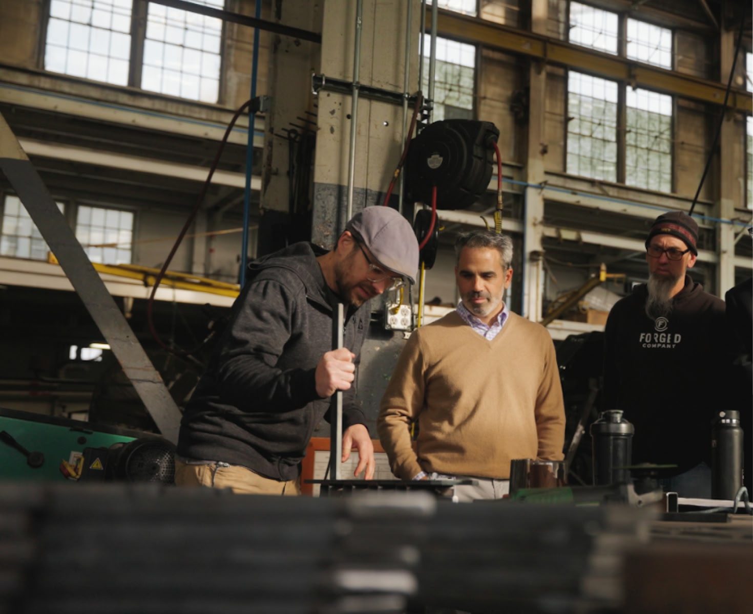 Four men stand in a sunlit industrial workshop, observing a project intently. The atmosphere is focused and collaborative, with tools visible on a table.