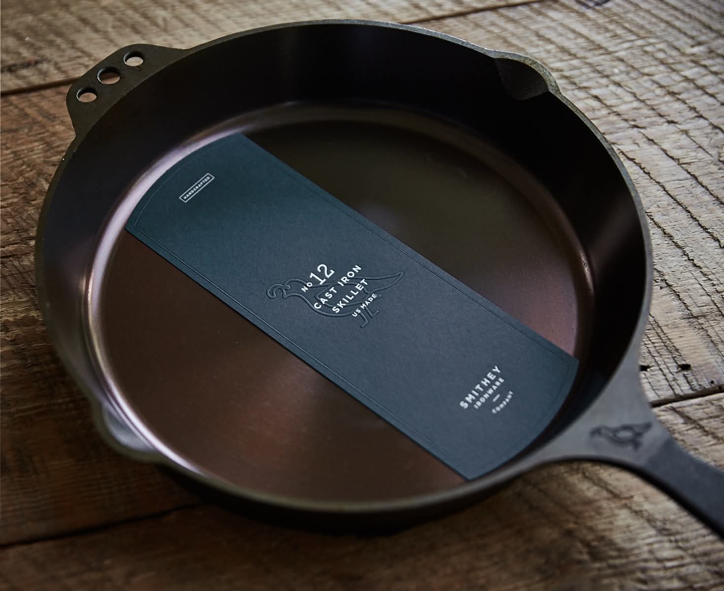 Cast iron skillet with a black label inside, placed on a rustic wooden surface.
