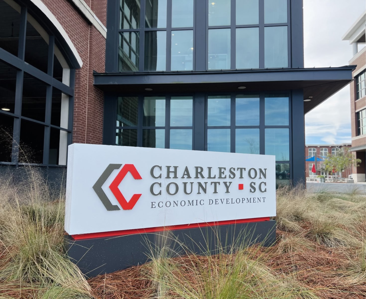 Sign for Charleston County Economic Development in front of a modern brick and glass building. Surrounded by grasses.
