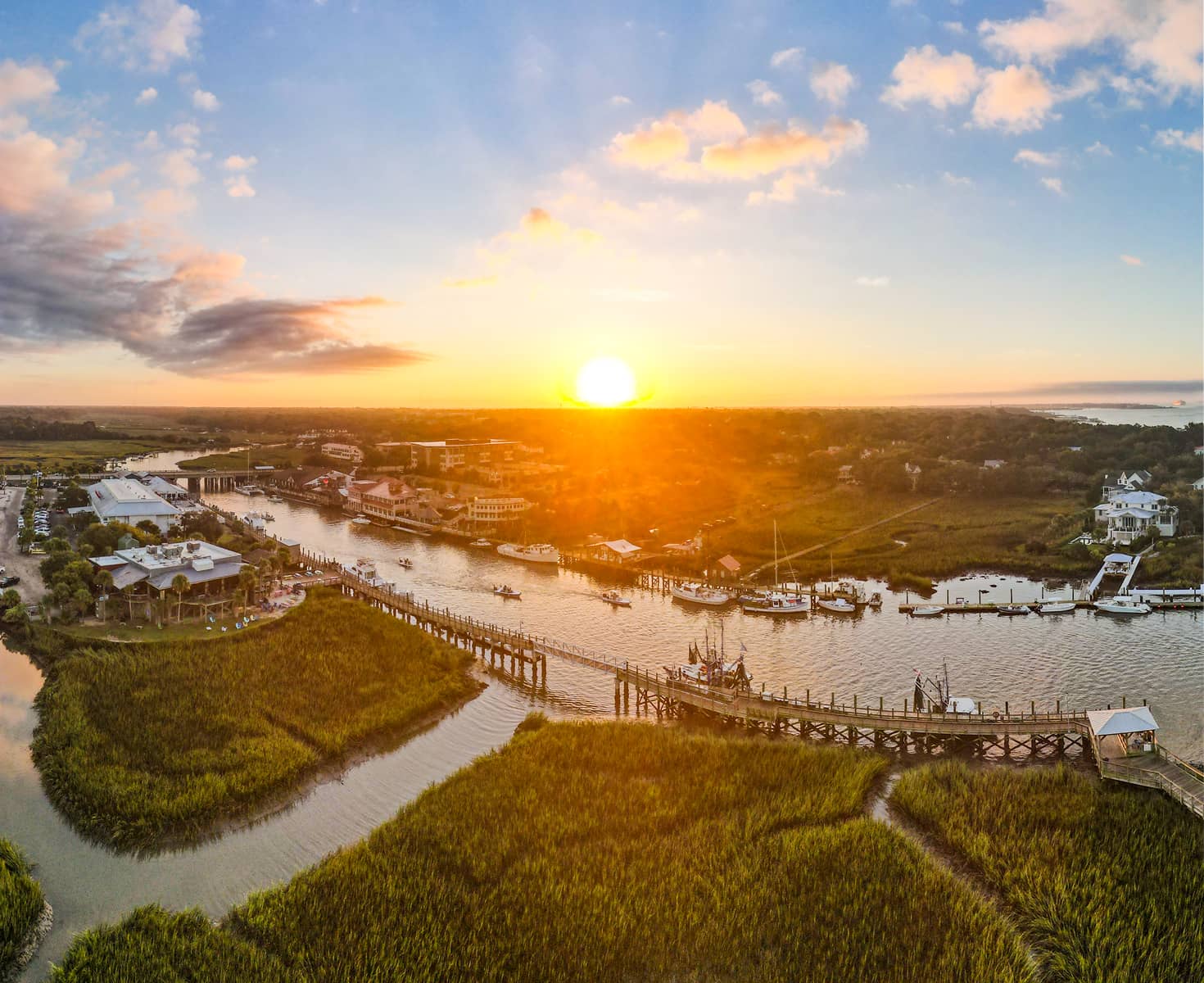 Aerial view of a vibrant sunset over a coastal town with a river, boats, and docks.