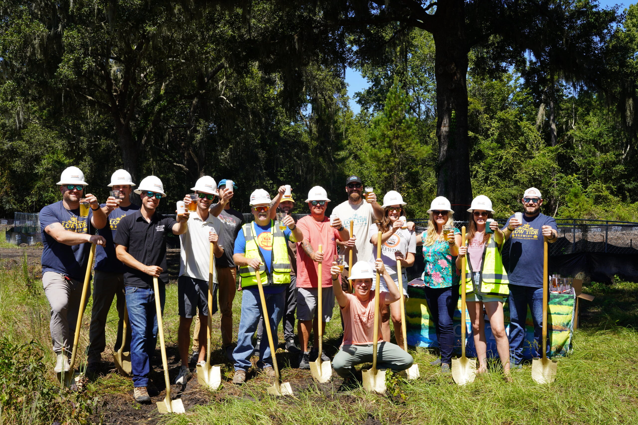 Group of team members wearing hard hats and holding shovels at a groundbreaking ceremony outdoors.